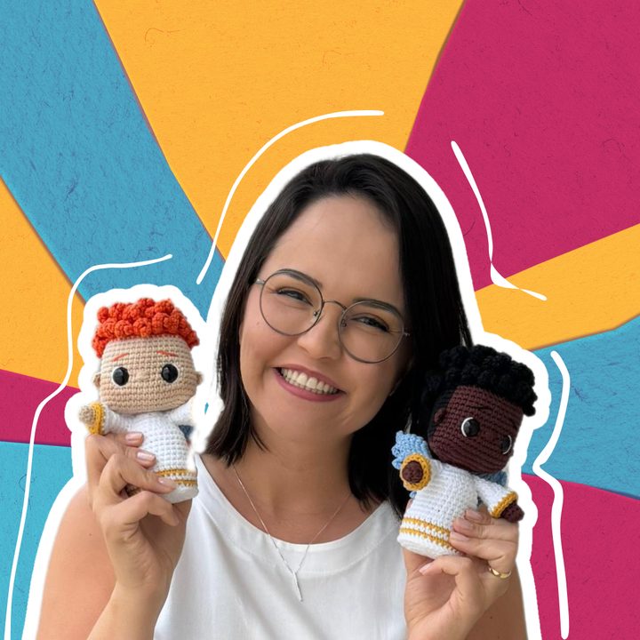 Ju Sanches smiling, holding two crocheted dolls, one in each hand